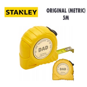 Puede incluir: Cinta m&eacute;trica Stanley amarilla con el texto "DAD" y "No One Measures Up To You". La cinta m&eacute;trica mide 5 metros de largo. El logotipo de Stanley es amarillo. El texto "ORIGINAL (METRIC)" est&aacute; encima de la medida de 5M.