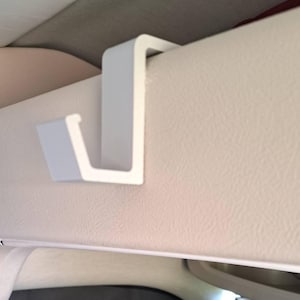 May include: White plastic hook designed to hang items from the visor of a car.