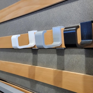 May include: Five hooks mounted on a wooden slat wall. Three hooks are white plastic and two are black plastic.