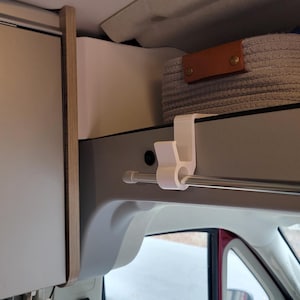 May include: White plastic hook mounted to a white ceiling with a silver metal rod attached. The hook is designed to hold items like clothes or towels.