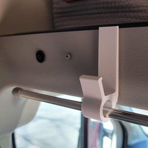 May include: White plastic hook mounted to a white ceiling with a silver metal rod running through it.
