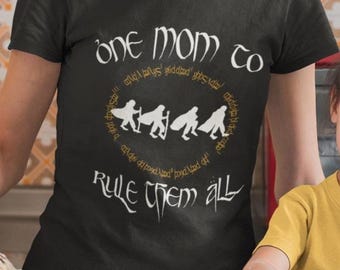May include: Black t-shirt with a gold design that says "One Mom to Rule Them All" with a circle of figures in the center. The figures are in a line and appear to be holding swords.