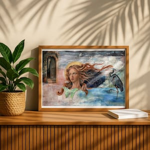 May include: A rectangular framed print featuring a surreal illustration of a person with long flowing auburn hair, a pale green moth resting on their chest, and a grey heron standing in blue water, set against a backdrop of a doorway and starry sky.
