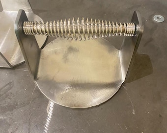 May include: A silver metal spring-loaded press with a round base and two vertical arms. The press is designed to be used for pressing objects.