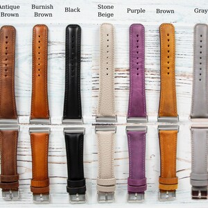 May include: A collection of leather watch bands in various colors, including Antique Brown, Burnish Brown, Black, Stone Beige, Purple, Brown, and Gray. Each band has a silver-tone buckle and is displayed on a light wood surface.