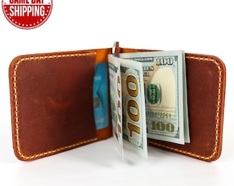 May include: A brown leather wallet with a money clip and a few bills sticking out. The wallet has a stitched edge and a yellow interior.