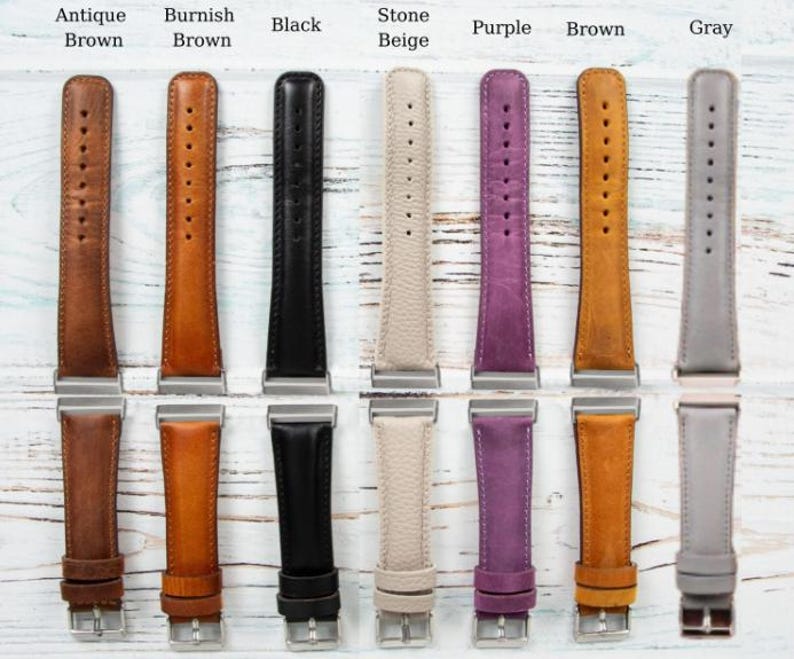May include: A collection of leather watch bands in various colors, including antique brown, burnish brown, black, stone beige, purple, brown, and gray. Each band has a silver-colored buckle and is displayed on a light-colored wooden surface.