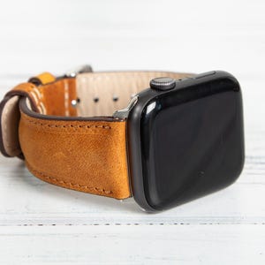 May include: A tan leather watch band with a black watch face. The band is made of a textured, light brown leather with a contrasting lighter interior. The watch face is rectangular with a black screen and a silver button.