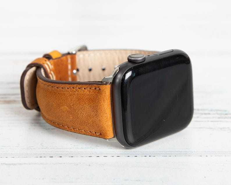 May include: A tan leather watch band with a black watch face. The band is made of a textured, light brown leather with a contrasting lighter interior. The watch face is rectangular with a black screen and a silver button.