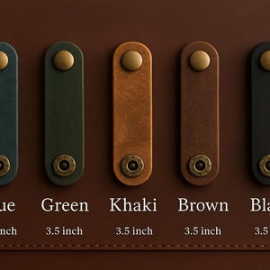 May include: Five leather pull tabs in blue, green, khaki, brown, and black, each with a brass rivet and a gold-colored stud. Each tab is 3.5 inches long. The tabs are displayed on a brown surface.