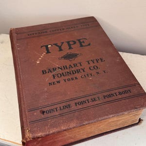 May include: A brown hardcover book titled Superior Copper-Mixed Type Barnhart Type Foundry Co. New York City, N. Y. The cover features black text and lines with the words Point-Line, Point-Set, and Point-Body printed at the bottom.