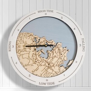 May include: A circular tide clock featuring a light blue background and a laser-cut wooden map overlay. The white outer frame displays the text HIGH TIDE, LOW TIDE, RISING, and FALLING, along with numerical markers from 0 to 5. Black clock hands are centred.