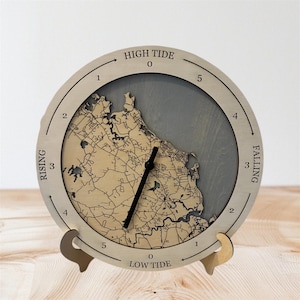 May include: A round wooden tide clock with a map design. The clock face has a light wood finish with a gray background. The clock hands are black. The words "HIGH TIDE" and "LOW TIDE" are visible.