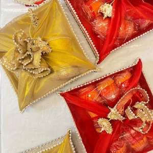 May include: Overhead view of several gift boxes wrapped in gold and red sheer fabric. The square boxes are decorated with bows, pearls, and gold embellishments. The gifts inside are visible through the transparent wrapping.