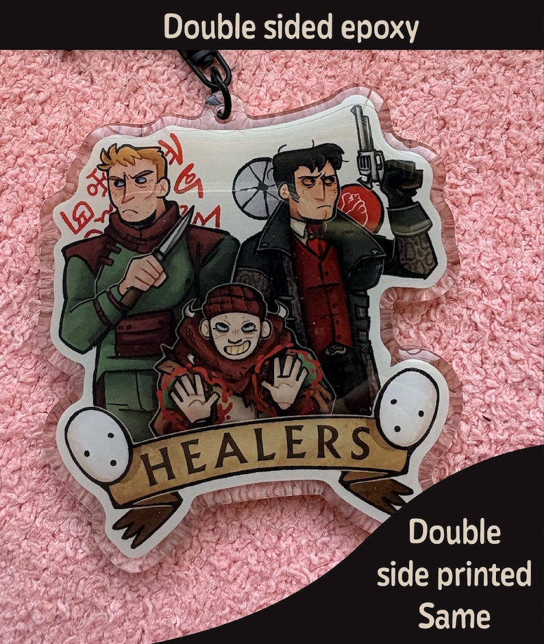 May include: A clear acrylic keychain featuring a double-sided epoxy finish with an illustration of three characters. Two figures stand behind a smaller character with a banner at the bottom that reads HEALERS. The text Double sided epoxy and Double side printed Same is visible.