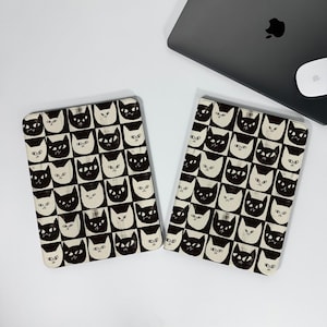 May include: Two rectangular cases with a repeating pattern of black and white cat faces. The cases are on a white surface, with a laptop and mouse in the background. The cat faces are in a grid pattern.