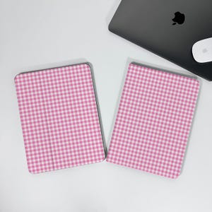 May include: Two pink and white gingham pattern tablet covers. The covers are rectangular with rounded corners. A laptop and mouse are in the background on a white surface.