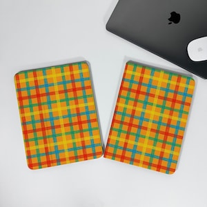 Può includere: Due quaderni rettangolari arancioni con un motivo a quadri colorati di linee rosse, gialle, verdi e blu. Un computer portatile nero e un mouse bianco sono sullo sfondo.