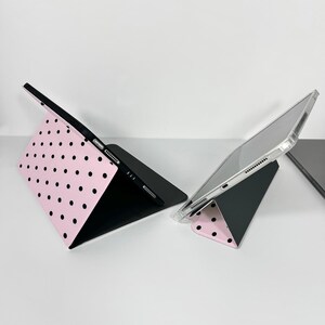 Op de afbeelding: Er worden twee tablethoezen getoond. E&eacute;n is open en toont een roze oppervlak met zwarte stippen. De andere hoes is gesloten, met een doorzichtige beschermhoes. Beide hoezen zijn aan de binnenkant zwart. De hoezen zijn ontworpen om een tablet te bevatten.