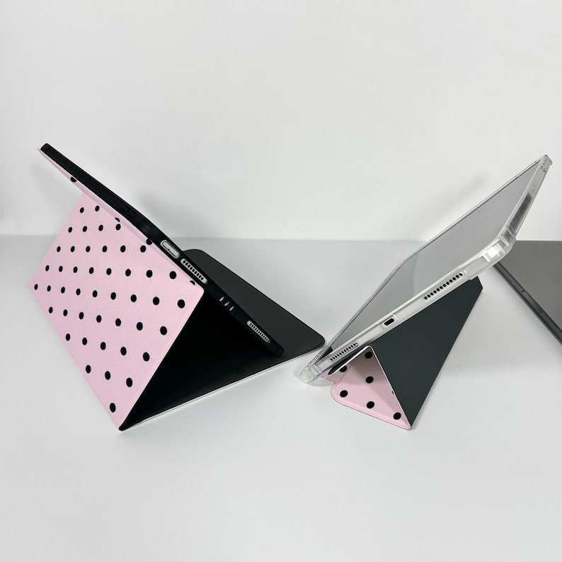 Op de afbeelding: Er worden twee tablethoezen getoond. E&eacute;n is open en toont een roze oppervlak met zwarte stippen. De andere hoes is gesloten, met een doorzichtige beschermhoes. Beide hoezen zijn aan de binnenkant zwart. De hoezen zijn ontworpen om een tablet te bevatten.