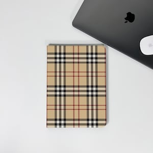 May include: A tan and plaid patterned tablet case with a black, white, and red grid design. The case is rectangular and sits on a white surface next to a laptop.