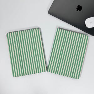May include: Two rectangular green and white striped laptop cases. The cases are side by side on a white surface. A black laptop and white mouse are in the background.