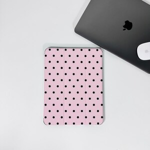 Op de afbeelding: Een roze tablethoesje met een zwart stippenpatroon. Een zwarte laptop en witte muis zijn op de achtergrond te zien. De hoes is rechthoekig en heeft een glad oppervlak. De stippen zijn gelijkmatig verdeeld.