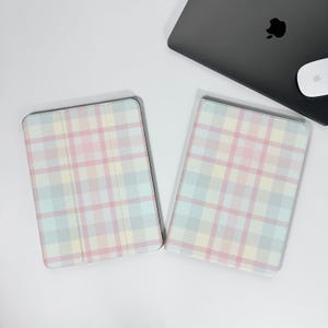 May include: Two pastel plaid tablet cases. The cases feature a pattern of pink, yellow, and blue squares. A black laptop and white mouse are in the background.