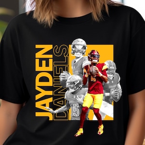 May include: Black t-shirt with a yellow and orange graphic of a football player in a red and gold uniform. The text "JAYDEN DANIELS" is printed in yellow on the shirt.