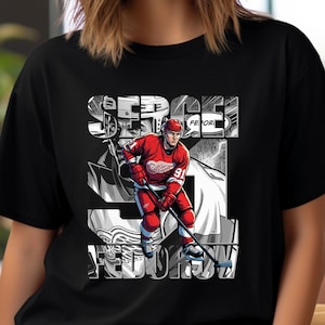 May include: Black t-shirt featuring a graphic of a hockey player in a red uniform with the number 91. The player is holding a hockey stick. The name "SERGEI FEDOROV" is printed in a stylized font.