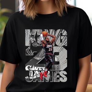 May include: A black short-sleeve t-shirt featuring a graphic print of a basketball player in a dark jersey with the number 23. The design includes the text KING JAMES in large block letters, a close-up portrait, and a dynamic action shot of the player.