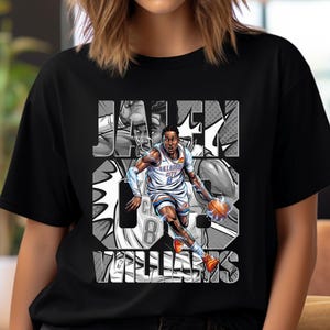Op de afbeelding: Zwart T-shirt met een afbeelding van een basketballer in een wit en blauw uniform, die een bal dribbelt. De naam en het rugnummer van de speler worden weergegeven in een gestileerd lettertype. Het shirt heeft een ronde hals.