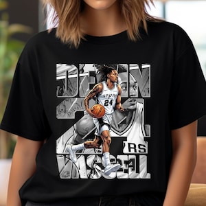 Pode incluir: Camiseta preta com um gráfico em tons de cinza de um jogador de basquete segurando uma bola. O jogador usa uma camisa com o número 24 e a palavra "SPURS". O design inclui o nome do jogador e o nome da equipe.