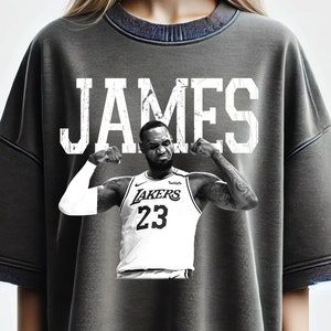 May include: A gray t-shirt with a white graphic of basketball player LeBron James wearing a Los Angeles Lakers jersey with the number 23. The text "JAMES" is printed in white above the graphic.