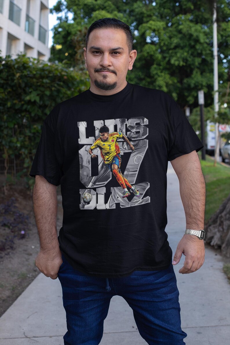 May include: Black t-shirt featuring a graphic of a soccer player in a yellow and orange uniform, with the name "Luis Diaz" and the number "7" in a stylized design. The player is depicted kicking a soccer ball.