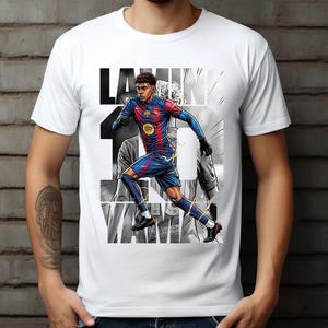 May include: White t-shirt featuring a graphic of a soccer player in a blue and red uniform, with the name "Lamine" and the number "10" in black. The design has a grayscale background.