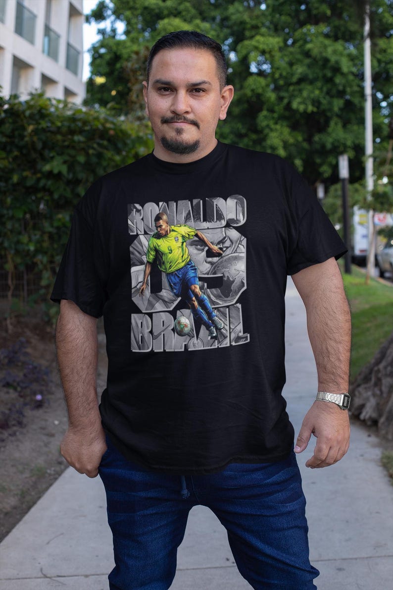 May include: Black t-shirt featuring a graphic of a soccer player in a yellow and blue uniform kicking a ball. The shirt has the text "RONALDO 9 BRAZIL" in a stylized font.