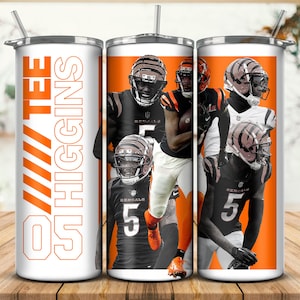 May include: A white and orange tumbler featuring a collage of football players in black and orange uniforms. The text "05 TEE HIGGINS" is vertically printed on the side. The tumbler has a silver lid and a straw.