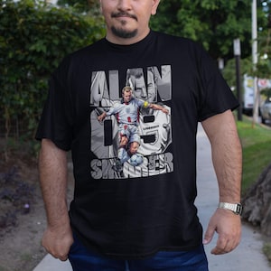 May include: Black t-shirt featuring a graphic of Alan Shearer in a soccer uniform, with the text "ALAN SHEARER" and the number 9. The shirt is a crew neck and is made of a soft material.