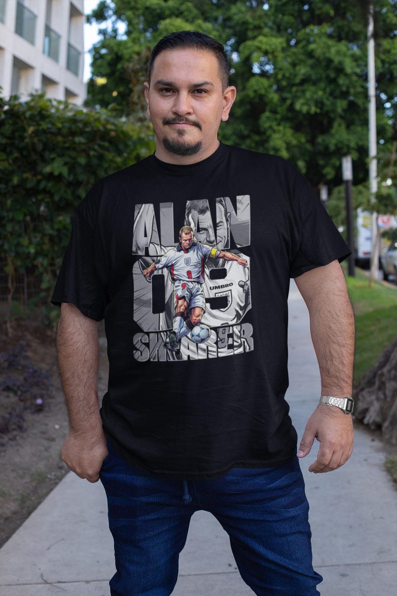 May include: Black t-shirt featuring a graphic of Alan Shearer in a soccer uniform, with the text "ALAN SHEARER" and the number 9. The shirt is a crew neck and is made of a soft material.