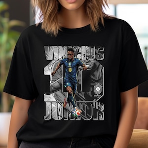 May include: Black t-shirt featuring a graphic of a soccer player in a blue uniform, with the name "VINICIUS JR" and the number "10" in white. The Brazilian flag and team logo are also visible.