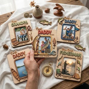 May include: Wooden photo frames with fishing-themed designs. The frames are engraved with the words "Best Grandpa Ever," "Best Daddy Ever," and "Our Best Fisherman Dad." Each frame holds a photograph and is decorated with fish and fishing-related elements.
