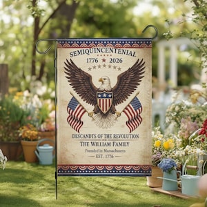 May include: A garden flag featuring a bald eagle with outstretched wings, holding American flags. The flag has the text "SEMIQUINCENTENIAL 1776 2026" and "DESCANDTS OF THE REVOLUTION THE WILLIAM FAMILY Founded in Massachusetts EST. 1776".