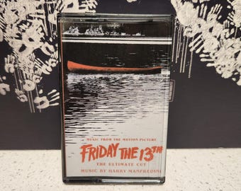 May include: A cassette tape with a red and white label. The label says "Music from the motion picture Friday the 13th The Ultimate Cut Music by Harry Manfredini".