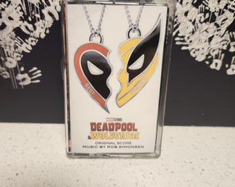 May include: A clear plastic case with a white background and a red and yellow heart-shaped design. The heart is split in half, with one half featuring a red and black Deadpool mask and the other half featuring a yellow and black Wolverine mask. The text "Best Friends" is printed on the Deadpool side of the heart. The text "Marvel Studios Deadpool & Wolverine Original Score Music by Rob Simonsen" is printed below the heart.