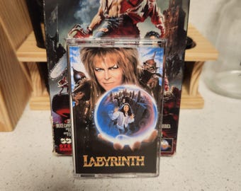May include: A vintage VHS tape of the movie "Army of Darkness" is behind a cassette tape of the movie "Labyrinth". The "Labyrinth" cassette features a movie poster image with the title at the bottom.