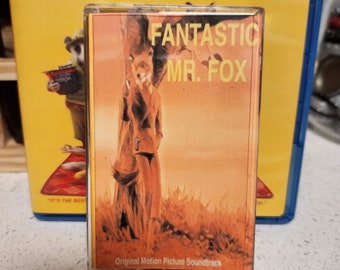 May include: A yellow and blue Blu-ray case with the title "Fantastic Mr. Fox" and the names of the actors, including George Clooney, Meryl Streep, Jason Schwartzman, Bill Murray, and Owen Wilson. The case is next to a smaller, orange and white cassette tape case with the same title, "Fantastic Mr. Fox". The cassette tape case has a picture of a fox standing in a forest.