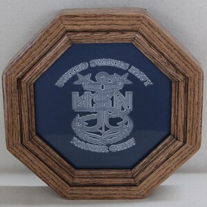Pode incluir: Uma moldura octogonal de madeira envolve um fundo azul marinho com um emblema prateado. O emblema apresenta as palavras "United States Navy" e "Master Chief" com uma âncora central e as letras "USN".