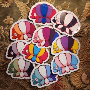 Puede incluir: Un conjunto de diez pegatinas de cochinillas de colores. Cada pegatina presenta una combinación de colores diferente de rayas y una pequeña 'x' en la cabeza. Las pegatinas están todas en posición enroscada.