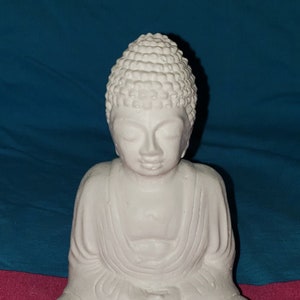 May include: White ceramic statue of a meditating Buddha. The statue is sitting in a lotus position with hands in the mudra gesture.